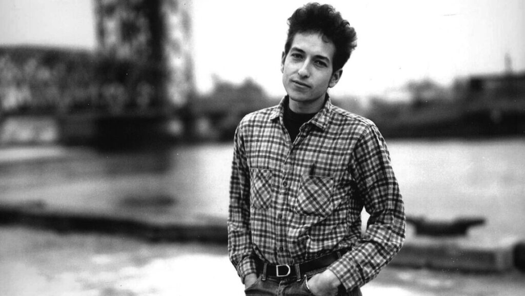 Bob Dylan | The Freewheelin’ Bob Dylan Bob Dylan, Freewheelin' era. Black and white portrait of the singer-songwriter wearing a plaid shirt.