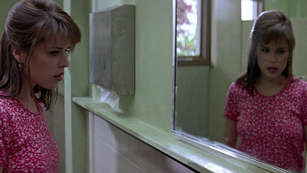 Scream | Wes Craven Neve Campbell in Scream movie scene. Sidney Prescott looking in mirror in restroom. Wes Craven horror film.