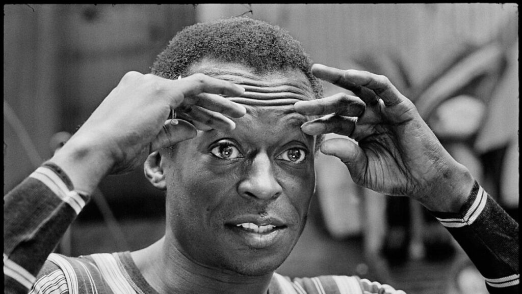 Miles Davis | In A Silent Way Black and white portrait of Miles Davis, jazz musician, with hands framing his face. In A Silent Way era.