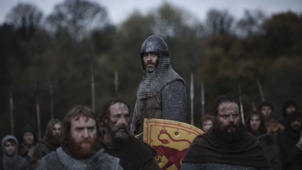 Outlaw King film still. Chris Pine as Robert the Bruce with his army, wearing armor and holding a shield.