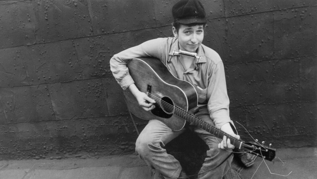 Bob Dylan, 1962. Black and white portrait of Bob Dylan playing guitar with harmonica. Folk music icon.