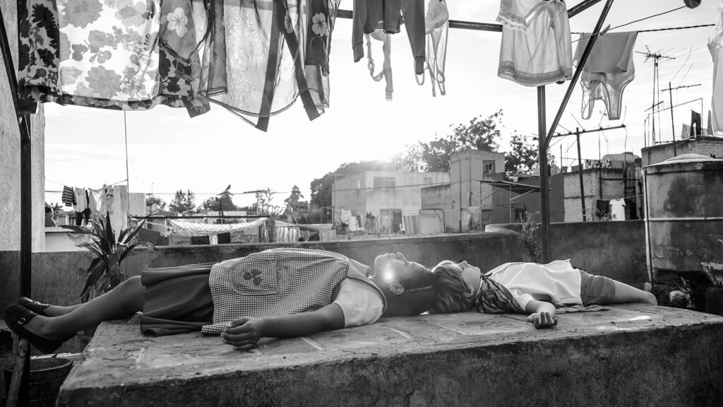 Black and white still from Alfonso Cuarón's Roma featuring two children laying on a rooftop.