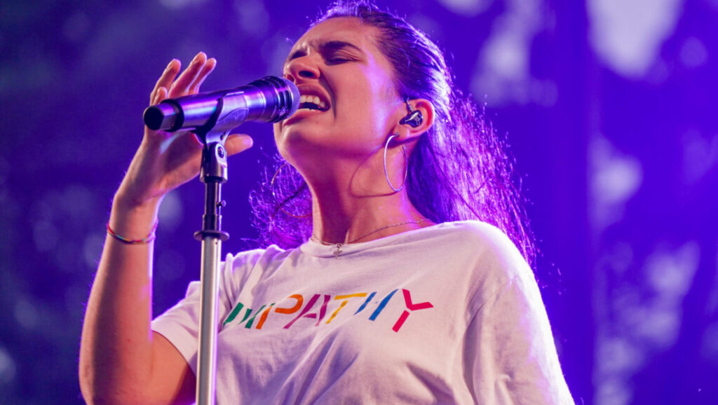 Alessia Cara | The Pains of Growing Alessia Cara performing live. The Pains of Growing era. Singer with microphone, lit with purple stage lights.