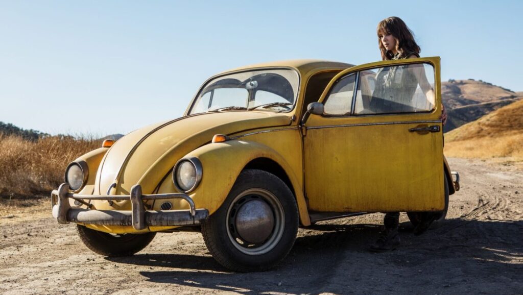 Bumblebee | Travis Knight Bumblebee movie: Yellow Volkswagen Beetle with a woman standing by the open door.