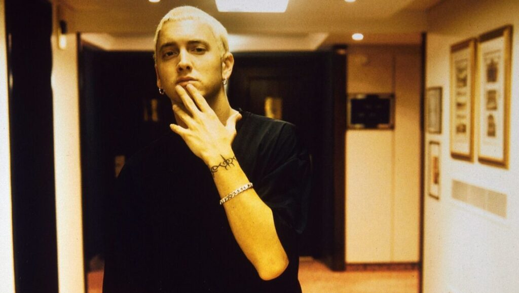 Eminem | The Slim Shady LP Eminem, the rapper, poses in a black shirt with blonde hair. Image relates to The Slim Shady LP.