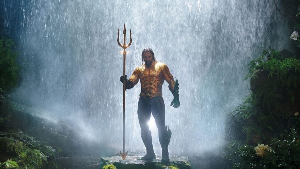 Aquaman | James Wan Jason Momoa as Aquaman in classic costume holding trident, waterfall background.