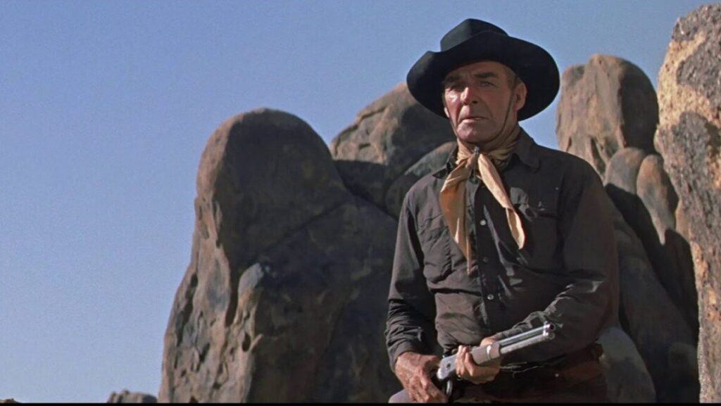 Still from Comanche Station (Budd Boetticher). Cowboy in black hat holds rifle in desert landscape. Classic Western film.