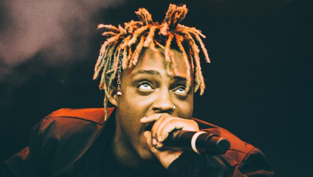 Juice WRLD performing rap music. Rapper with dreadlocks holds a microphone. 2018 rap releases.