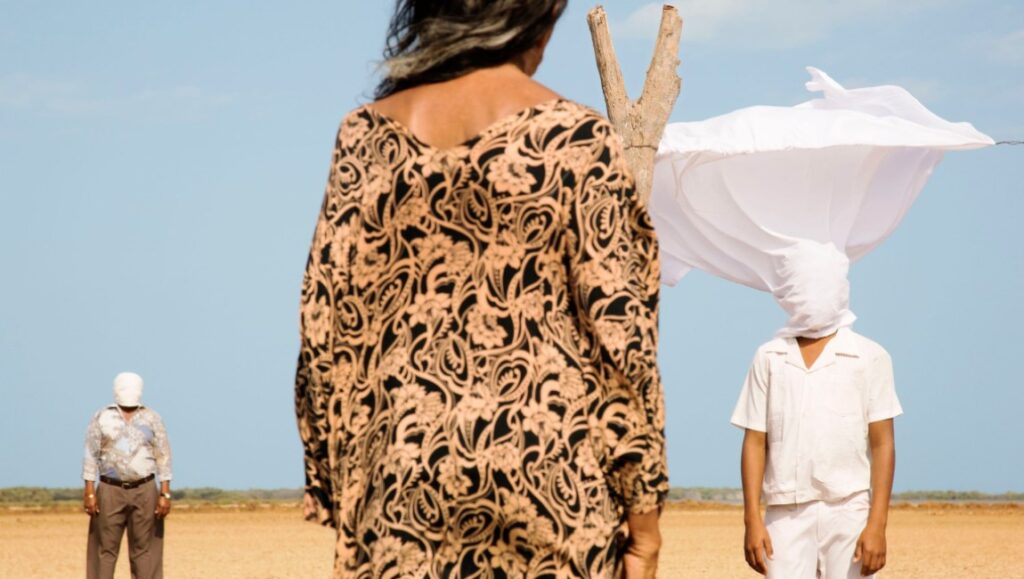 Birds of Passage | Ciro Guerra & Cristina Gallego Birds of Passage film still. Woman in patterned dress, figures with covered faces in a desert landscape.