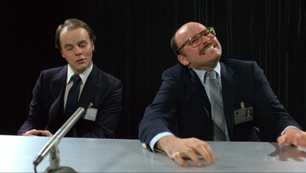 Scanners movie scene. Man with glasses strains, another looks on. David Cronenberg film.