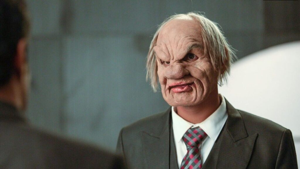 Dhayam film backdrop. Man in suit with scary mask. Kannan Rangaswamy film.