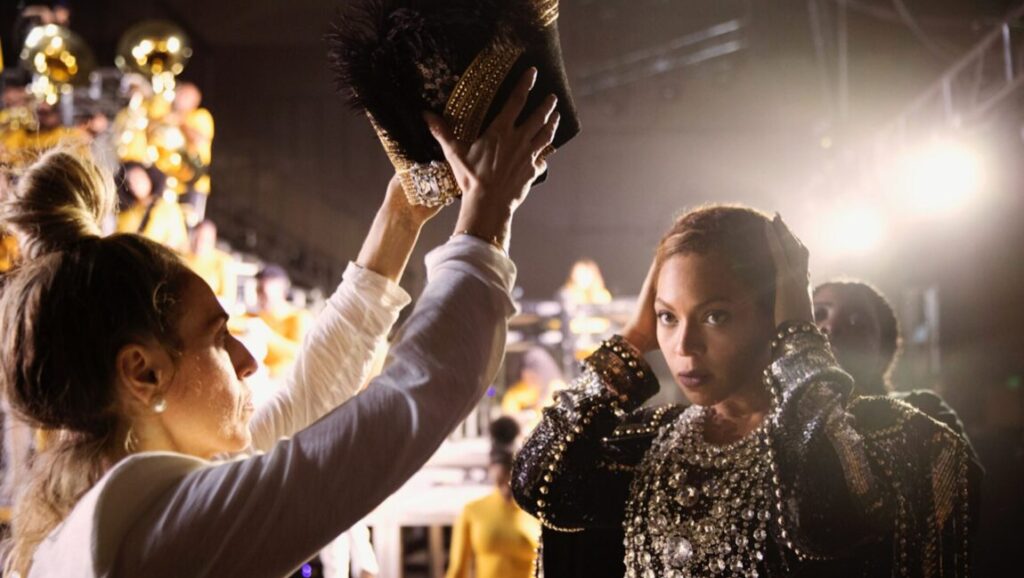 Homecoming: A Film by Beyoncé | Beyoncé & Ed Burke Beyoncé in Homecoming film. Backstage photo with marching band. Beyoncé wearing a jeweled outfit.