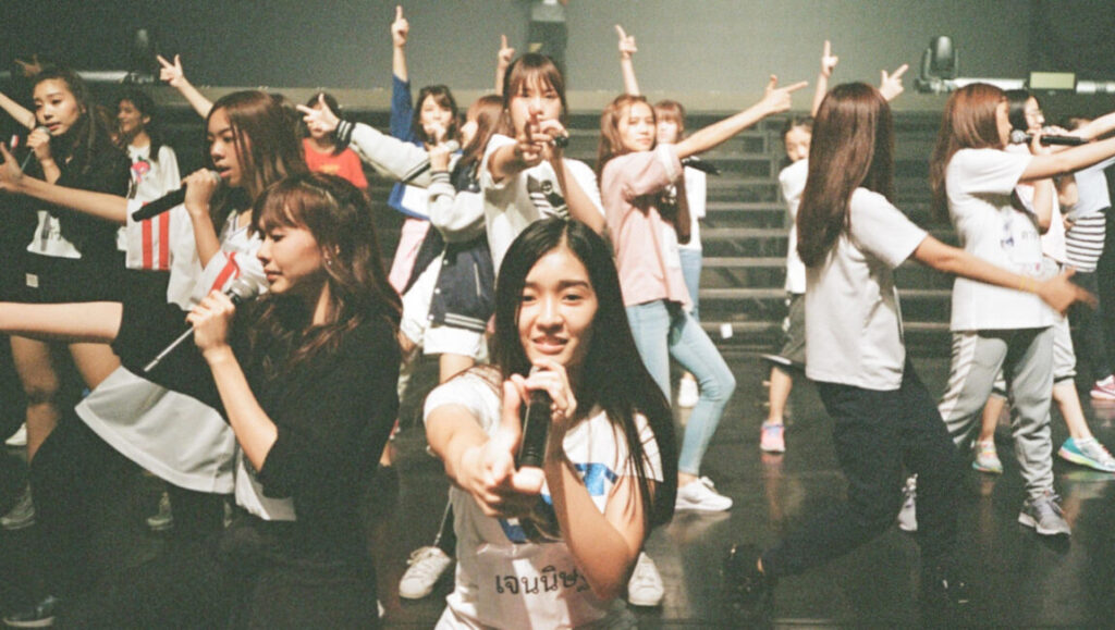 BNK48 performing Girls Don't Cry. Thai idol group on stage with microphones. Nawapol Thamrongrattanarit film.