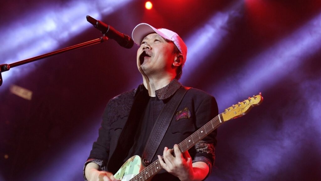 Cui Jian, Chinese rock musician, performs on stage with guitar and microphone. Rock 'n' Roll on the New Long March.