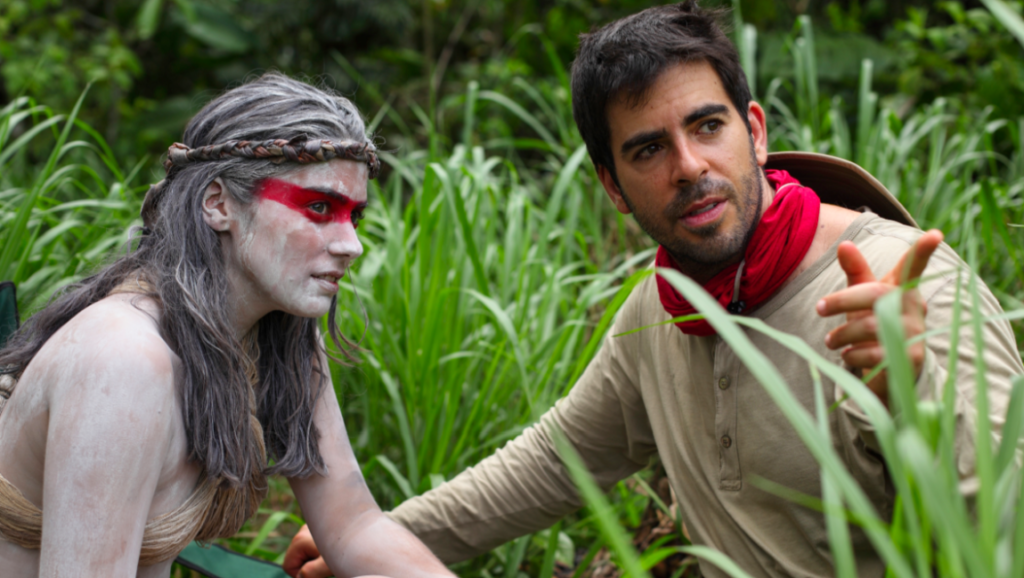 Eli Roth directs actors in The Green Inferno. Horror film scene with tribal makeup and jungle backdrop.