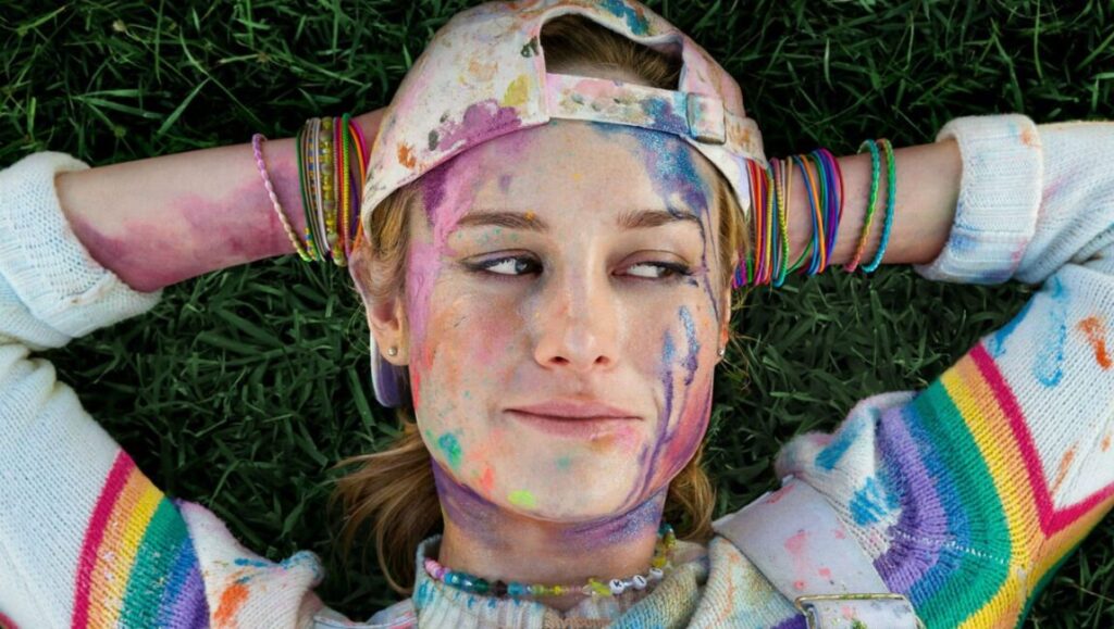 Unicorn Store | Brie Larson Brie Larson in Unicorn Store. Woman covered in paint lying on grass. Colorful, whimsical movie scene.