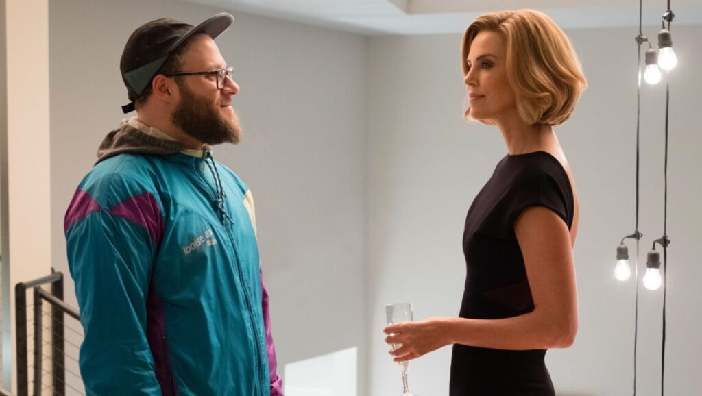 Long Shot movie scene: Seth Rogen and Charlize Theron. Rogen wears a colorful jacket and Theron, an elegant black dress.