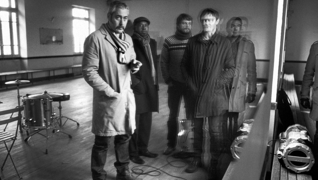 Like Only Lovers Can: A Decade of Tindersticks Black and white shot of the Tindersticks band, promoting Like Only Lovers Can: A Decade of Tindersticks.