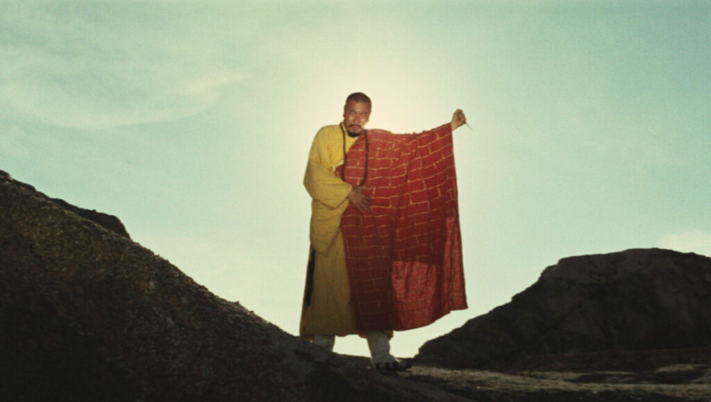King Hu's A Touch of Zen film still. Monk in yellow robes holds a red brick-patterned cloth against a sunny sky.