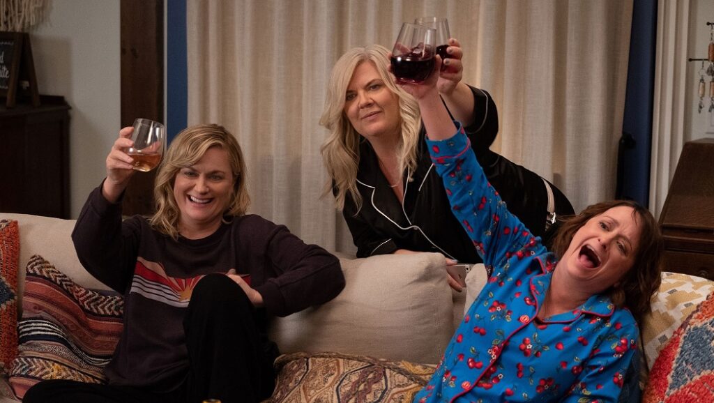 Amy Poehler's Wine Country cast cheers with wine glasses on a couch. Girls' night in.