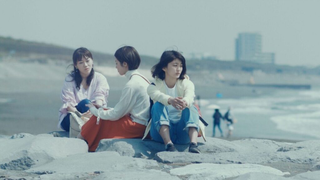 Japan Cuts 2019 film still: Three women sit on rocks near the beach. Japanese cinema.