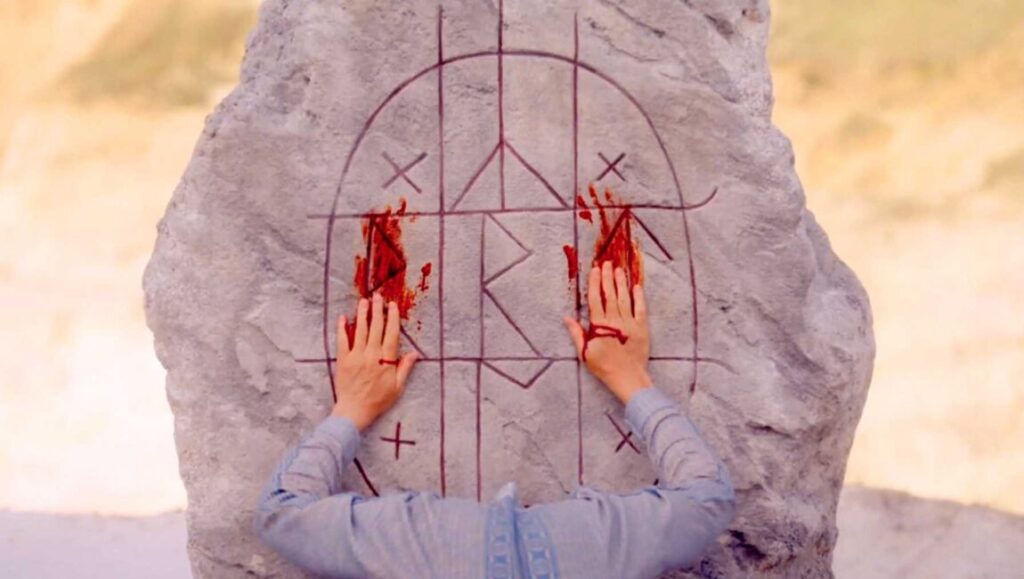 Midsommar movie scene. Bloody hands on runestone with ritualistic markings. Ari Aster film.