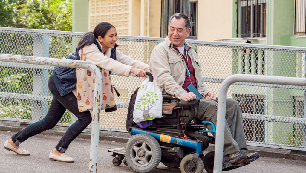 Still Human film scene: Woman pushing man in wheelchair. Disability and caregiving.
