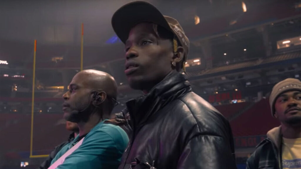 Travis Scott: Look Mom I Can Fly | White Trash Tyler Travis Scott at Look Mom I Can Fly. Rapper wearing a hat and leather jacket at a stadium.