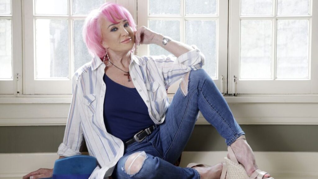 Rooted & Restless: Woman with pink hair, ripped jeans, and a striped shirt sitting by a window. Issue 6 fashion editorial.