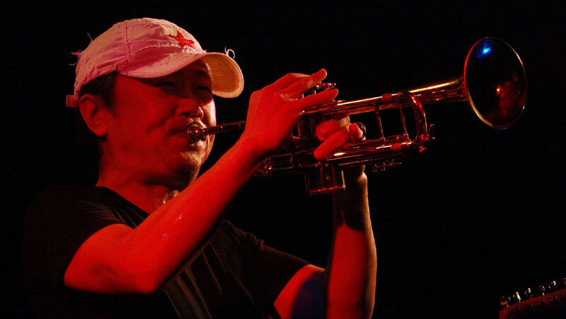 Cui Jian | Show You Colour Cui Jian playing trumpet. Musician performing Show You Colour live. Red lighting.