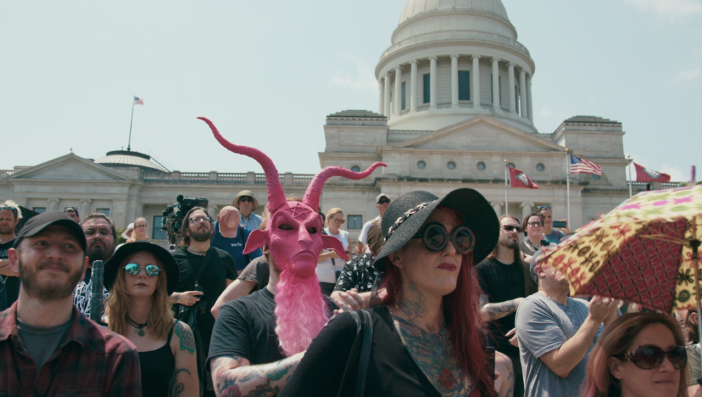 Hail Satan? | Penny Lane Hail Satan? protest. Crowd with a pink Baphomet mask in front of a capitol building. Satanic Temple activism.