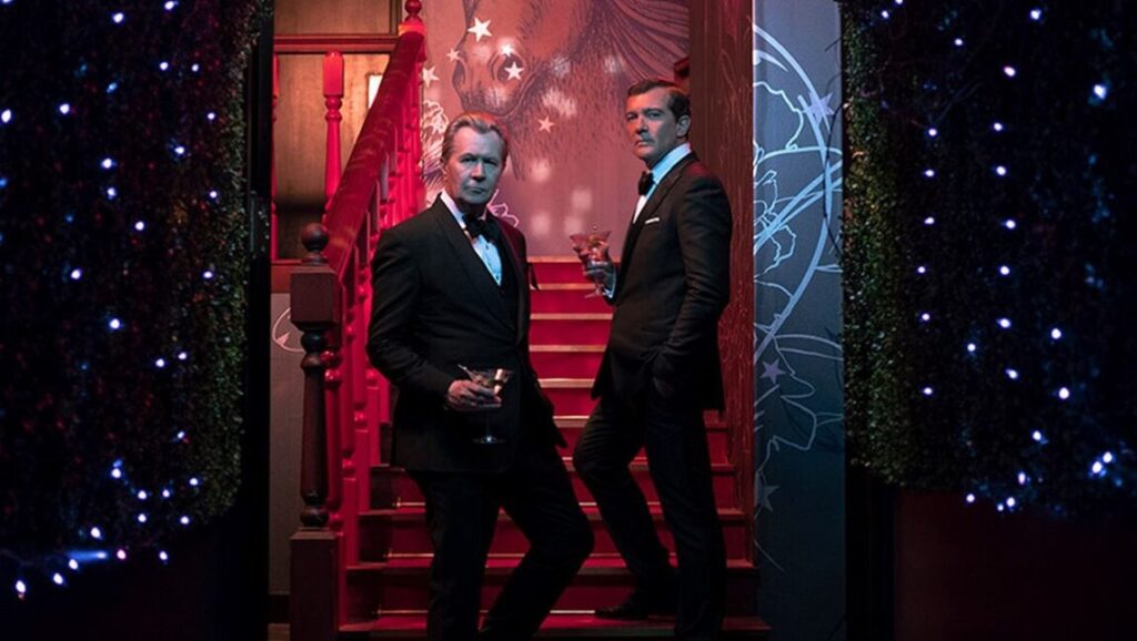 Gary Oldman and Antonio Banderas in The Laundromat movie. Men in black suits holding cocktails.