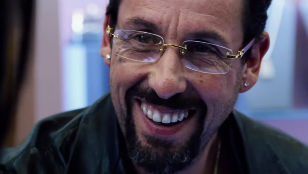 Adam Sandler in Uncut Gems at the New York Film Festival 2019. Close-up of Sandler smiling with gold glasses.