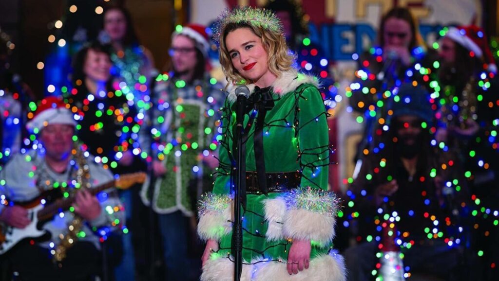 Last Christmas | Paul Feig Emilia Clarke in Last Christmas movie. Festive scene with Christmas lights and a choir. Paul Feig film.