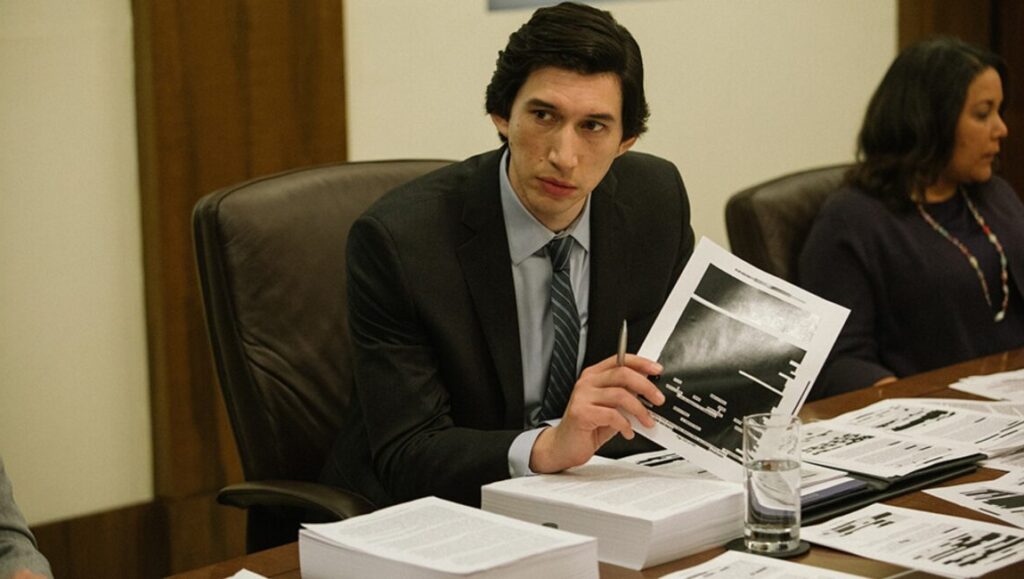 The Report | Scott Z. Burns Adam Driver in The Irishman, a Martin Scorsese film. Driver holds a document at a table with papers.