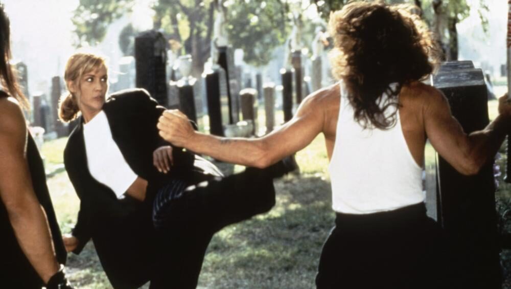 Excessive Force II: Force on Force movie scene. Woman in suit kicks man in tank top in a graveyard. Action film.
