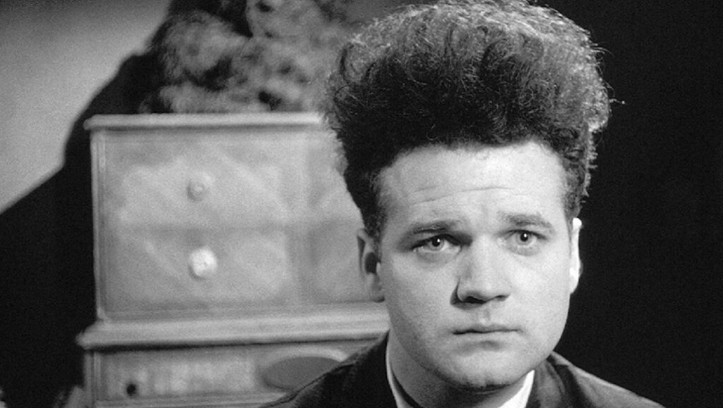 Henry Spencer in David Lynch's *Eraserhead*. Black and white film still with a man and a dresser. Cult classic.