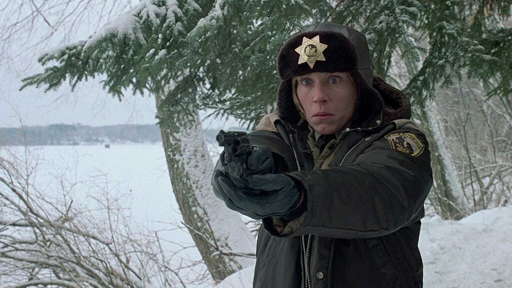 Fargo Review | Joel & Ethan Coen Fargo movie scene: Marge Gunderson (Frances McDormand) in winter gear, holding a gun in the snowy landscape.