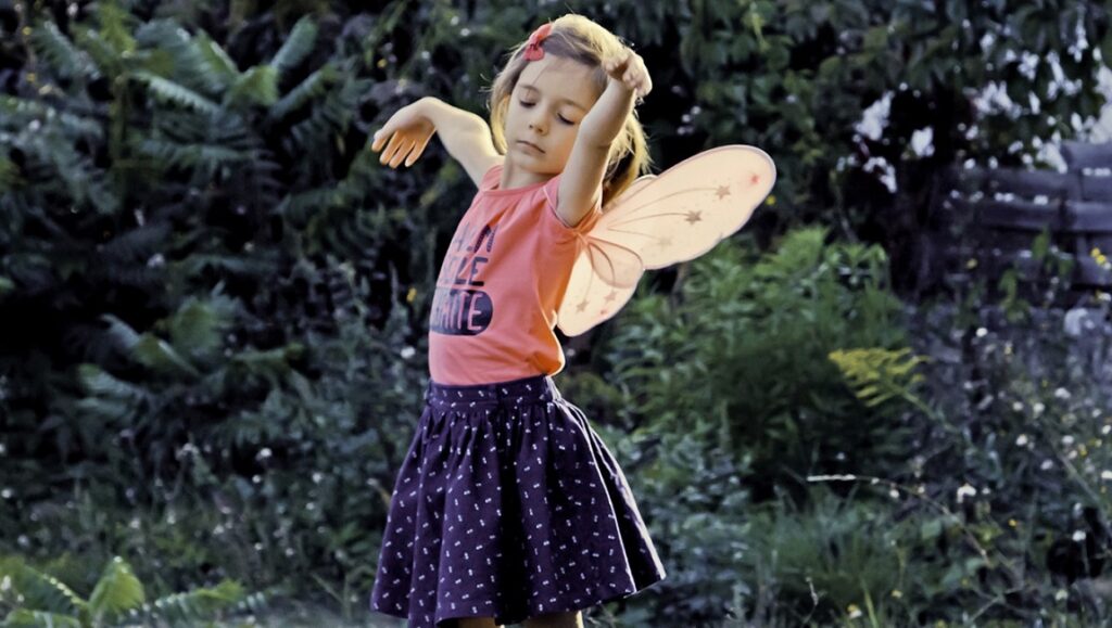 Little girl with fairy wings dancing in a garden. Sébastien Lifshitz film still. Child with wings.