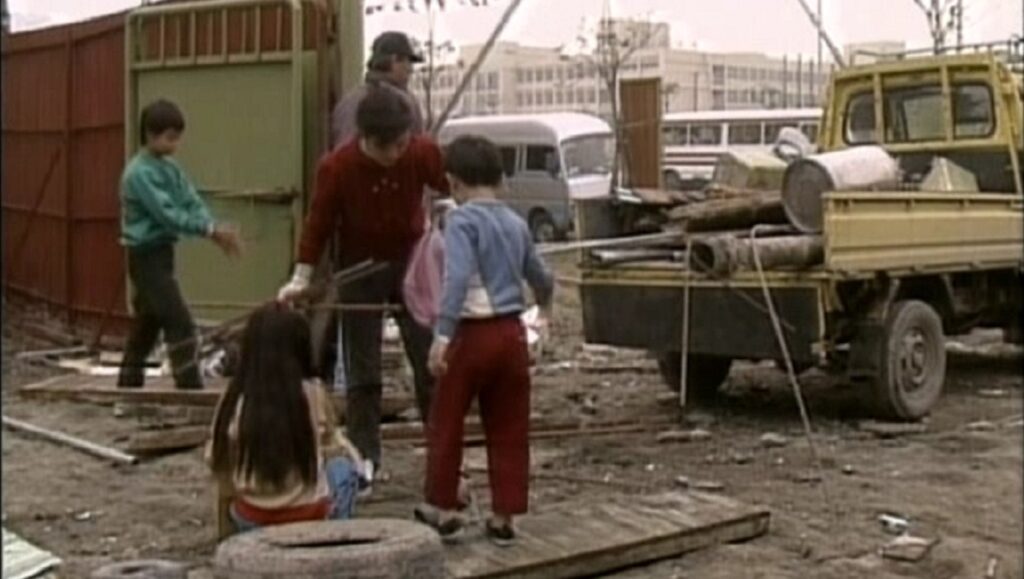 Give Me a Home | Tsai Ming-liang Give Me a Home film scene: Children and a man near a truck filled with materials. Urban landscape.