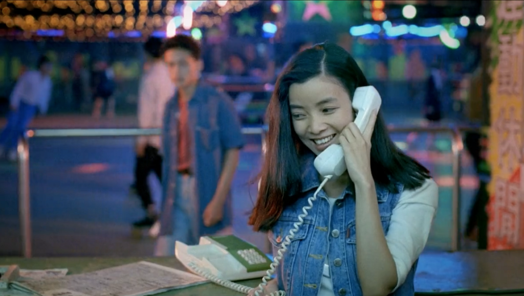 Still from Rebels of the Neon God featuring a woman smiling while using a landline phone in a vibrant, neon-lit setting.