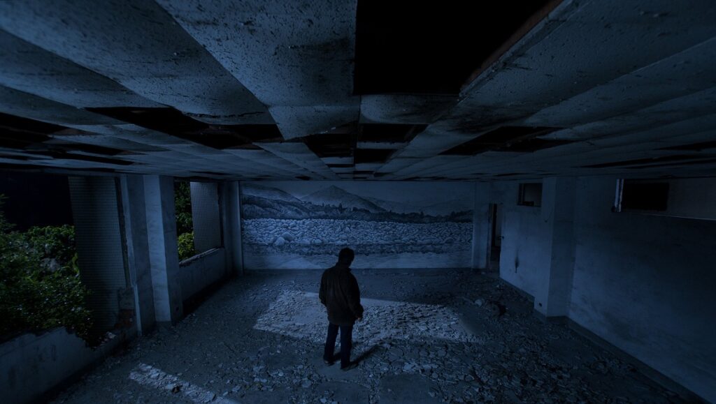 Stray Dogs | Tsai Ming-liang Stray Dogs film still. Tsai Ming-liang's Journey to the West. Man in derelict building, mural backdrop. Dark, moody.