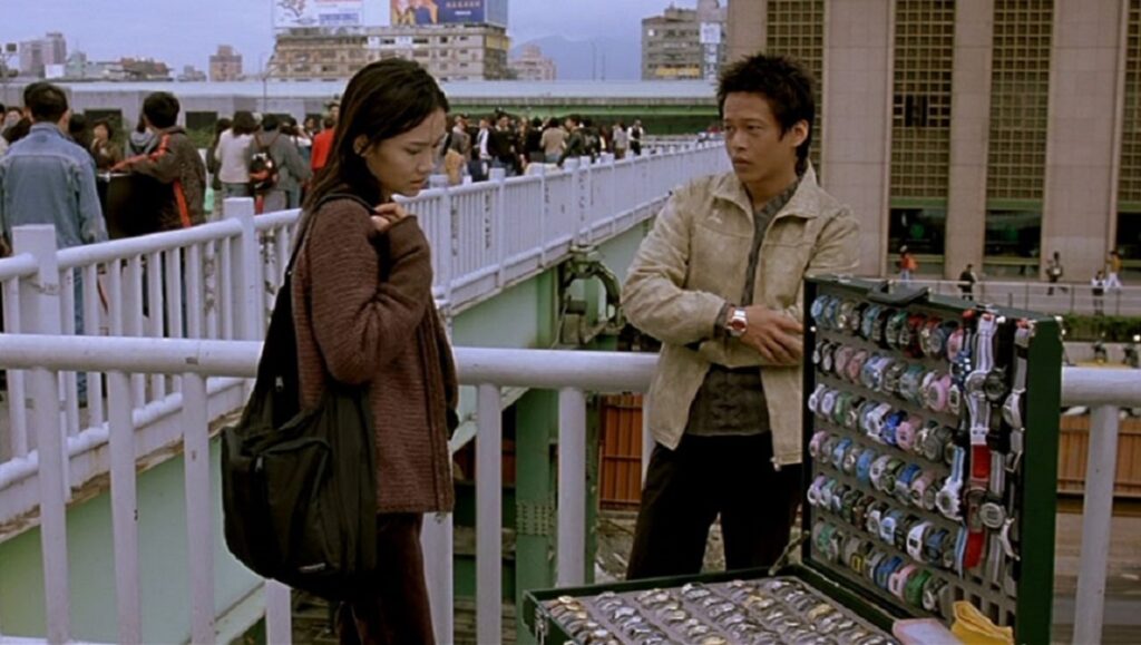 What Time is It There? & The Skywalk is Gone | Tsai Ming-liang What Time Is It There? film still. Man selling watches to a woman on a bridge. Tsai Ming-liang movie.