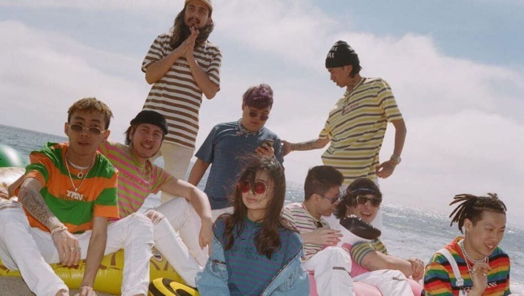 88rising's Head in the Clouds artists. Group of musicians on a beach, wearing colorful streetwear.