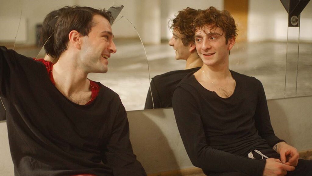 And Then We Danced film still. Two male dancers in practice clothes, looking at each other in a dance studio.