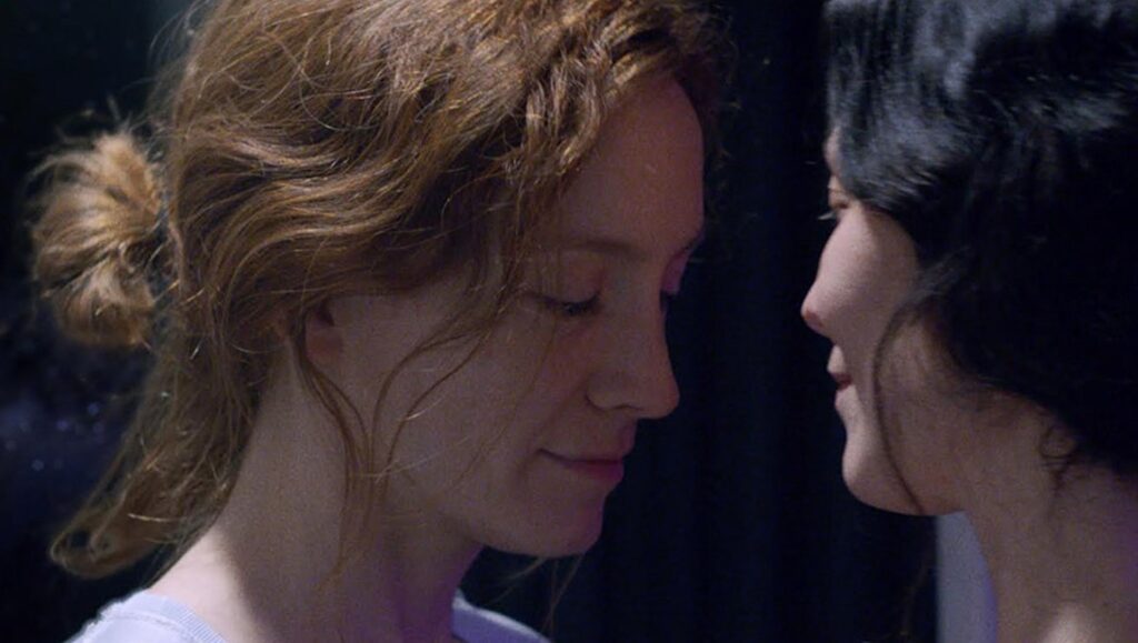 Aniara film still: Two women face each other closely. One with auburn hair, the other with dark hair.