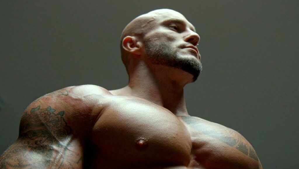 A Skin So Soft | Denis Côté A Skin So Soft film still: Muscular, tattooed man with shaved head looking up. Denis Côté film.