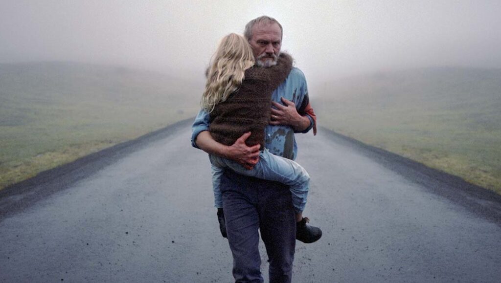 A White, White Day | Hlynur Pálmason A White, White Day film still. Man carries a child on a foggy road. Hlynur Pálmason movie.