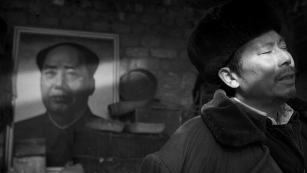 Bangzi Melody | Zheng Dasheng Bangzi Melody still: Zheng Dasheng film shows a man singing near a Mao Zedong portrait. Black and white.