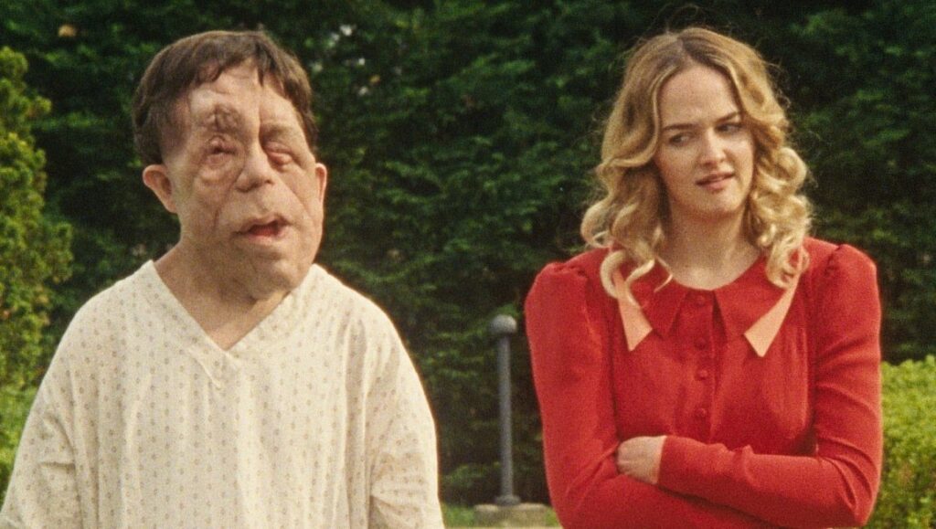 Chained for Life | Aaron Schimberg Still from Chained for Life film. Man with facial differences and a woman in a red dress stand outside.